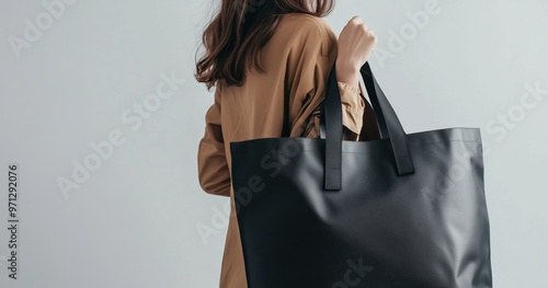 A stylish woman holding a sleek black tote bag against a minimalist background, showcasing modern fashion and elegance.