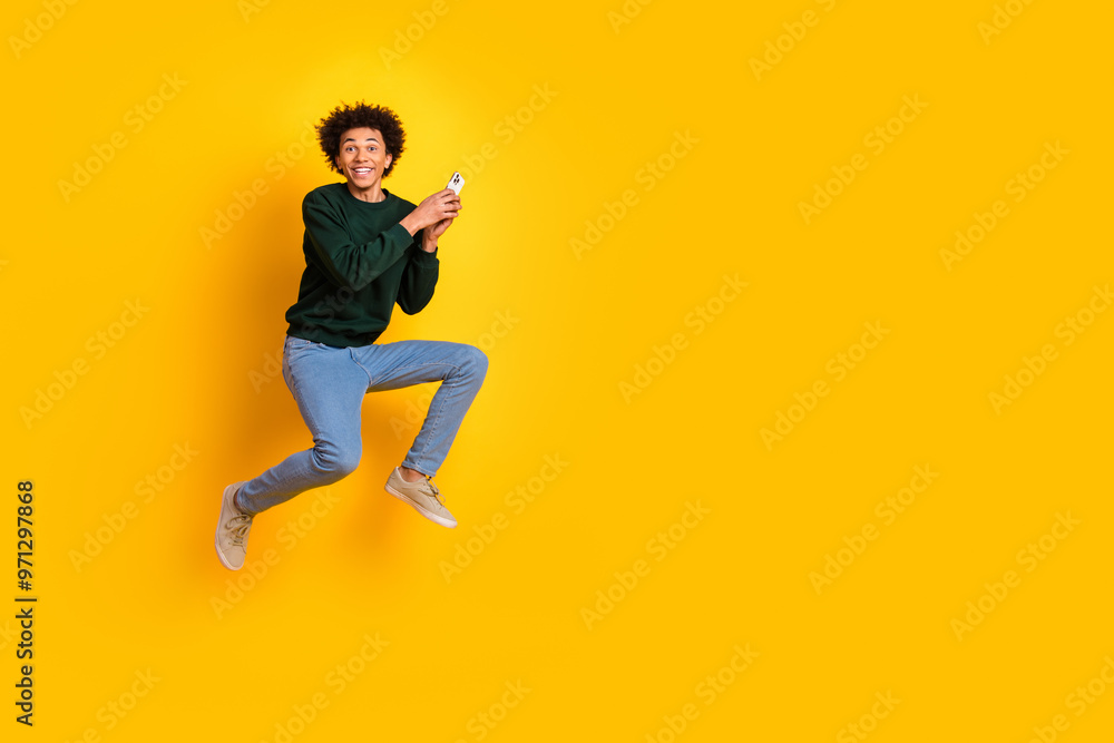 Full size photo of nice young man jump hold smart phone wear pullover isolated on yellow color background Full size photo of nice young man jump hold smart phone wear pullover isolated on yellow color background