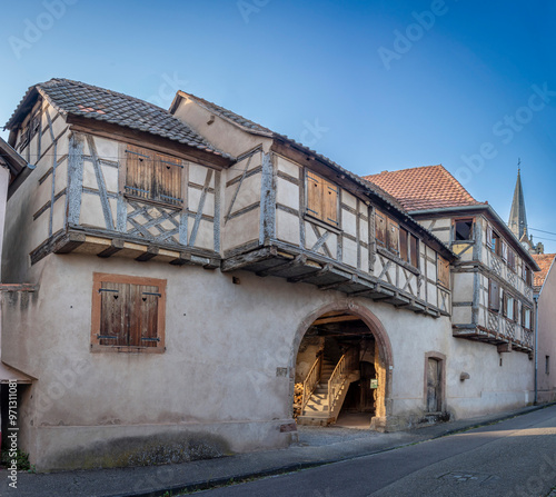 Bernardswiller, France - 09 04 2023: View of the facade of a typical half-timbered house, its courtyard and the church bell tower. photo