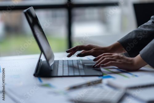 Businesswoman analyzing data on tablet with financial charts and documents at office desk