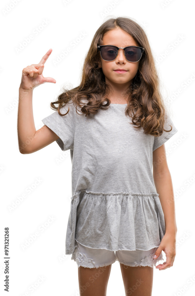 Brunette hispanic girl wearing sunglasses smiling and confident gesturing with hand doing size sign with fingers while looking and the camera. Measure concept. Brunette hispanic girl wearing sunglasses smiling and confident gesturing with hand doing size sign with fingers while looking and the camera. Measure concept.