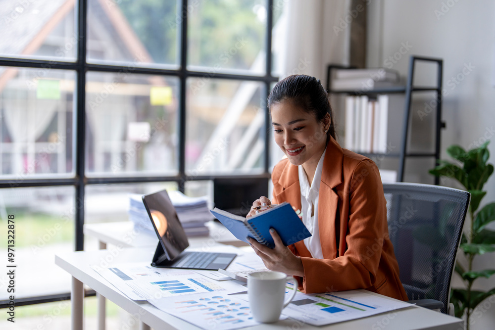 Businesswoman smiling and taking notes about financial chart in modern office Businesswoman smiling and taking notes about financial chart in modern office