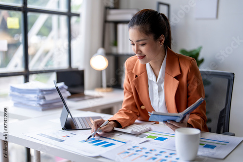 Young asian businesswoman analyzing financial chart using digital tablet and calculator in office photo