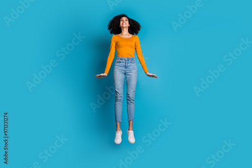 Full length photo of lovely young lady jump look up empty space dressed stylish yellow garment isolated on blue color background