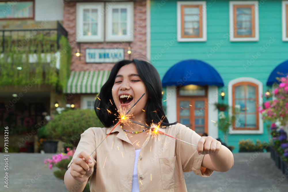 Fototapeta premium cheerful young asian woman holding sparkler to celebrate new year eve with garden party standing over colorful vintage house yard