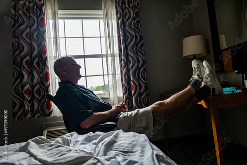 Solomons, Maryland USA A man sits by the window in a motel room with his feet up on the table. photo