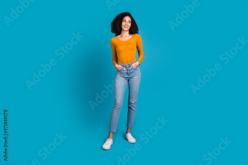 Full length photo of lovely young lady hands pockets look empty space dressed stylish yellow garment isolated on blue color background