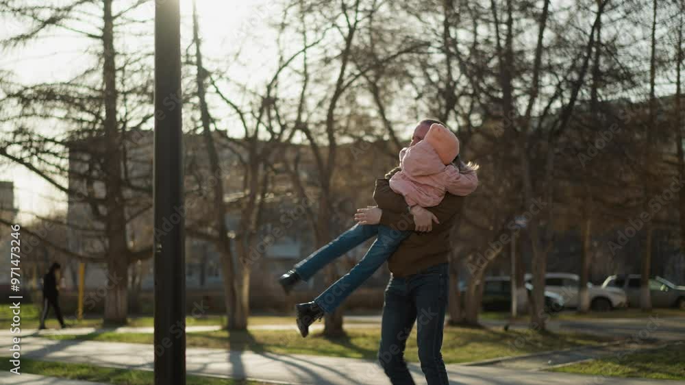 A man wearing a brown jacket and blue jeans joyfully carrying and spinning a little girl in a pink cap and jacket in a sunlit park. a playful and heartwarming moment of father-daughter bonding A man wearing a brown jacket and blue jeans joyfully carrying and spinning a little girl in a pink cap and jacket in a sunlit park. a playful and heartwarming moment of father-daughter bonding