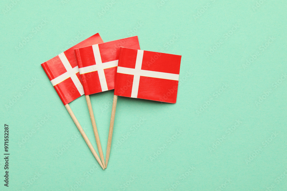Fototapeta premium Small paper flags of Denmark on turquoise background, top view. Space for text