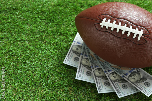 Fotografi American football ball and dollar banknotes on green grass outdoors, space for t