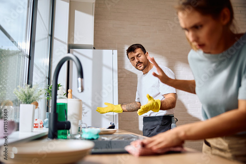 Fotografie Young man having  argument with is girlfriend while doing  dishes in  kitchen