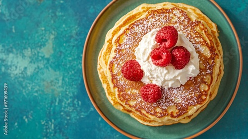 Golden brown pancakes with fresh raspberries and whipped cream, set against a rich teal background for a luxurious look photo