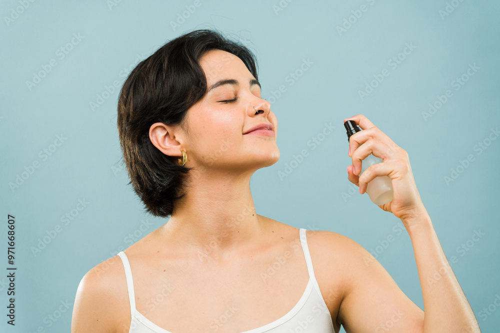 Smiling young woman with short hair applies some perfume on her neck with her eyes closed Smiling young woman with short hair applies some perfume on her neck with her eyes closed