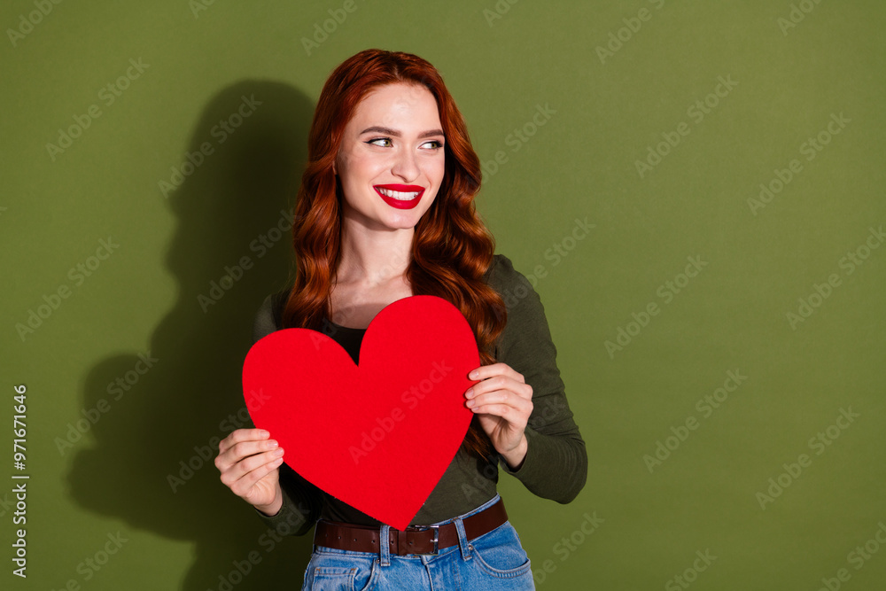 Photo of girlish lovely lady dressed shirt rising big red heart looking empty space isolated green color background Photo of girlish lovely lady dressed shirt rising big red heart looking empty space isolated green color background