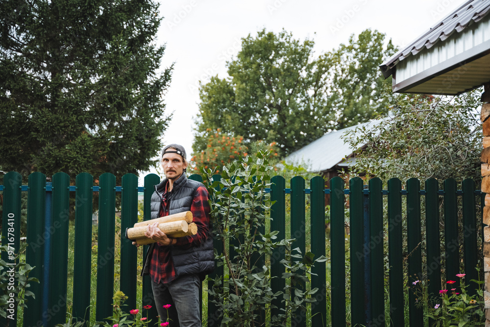 A man carries firewood through a charming garden surrounded by lush greenery, creating a peaceful and cozy atmosphere for relaxation A man carries firewood through a charming garden surrounded by lush greenery, creating a peaceful and cozy atmosphere for relaxation