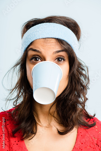 Funny, crazy and woman with coffee cup in studio for fitness with retro headband for workout. Caffeine addict, goofy and female athlete drinking takeaway cappuccino with vintage exercise fashion. photo