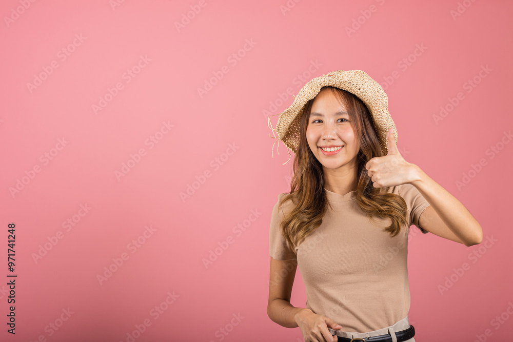 Portrait Asian young woman is smiling and giving a thumbs up while wearing a hat in studio shot isolated pink background, which gives it a cheerful and positive vibe, excellent sign Portrait Asian young woman is smiling and giving a thumbs up while wearing a hat in studio shot isolated pink background, which gives it a cheerful and positive vibe, excellent sign