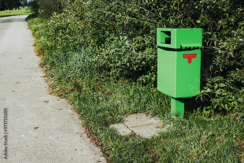 Public dog poop bag dispenser at the side of a street. Green Garbage bin with red doggy bags. Public service program to keep dog waste from streets and nature. Selective focus. Lucerne, Switzerland.