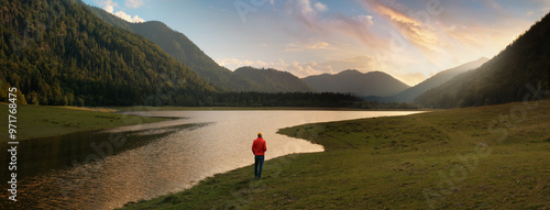 Hiker standing at a lake and enjoying the vastness of the majestic landscape in the Alps. Real solitude at sunset and experiencing nature to the fullest.