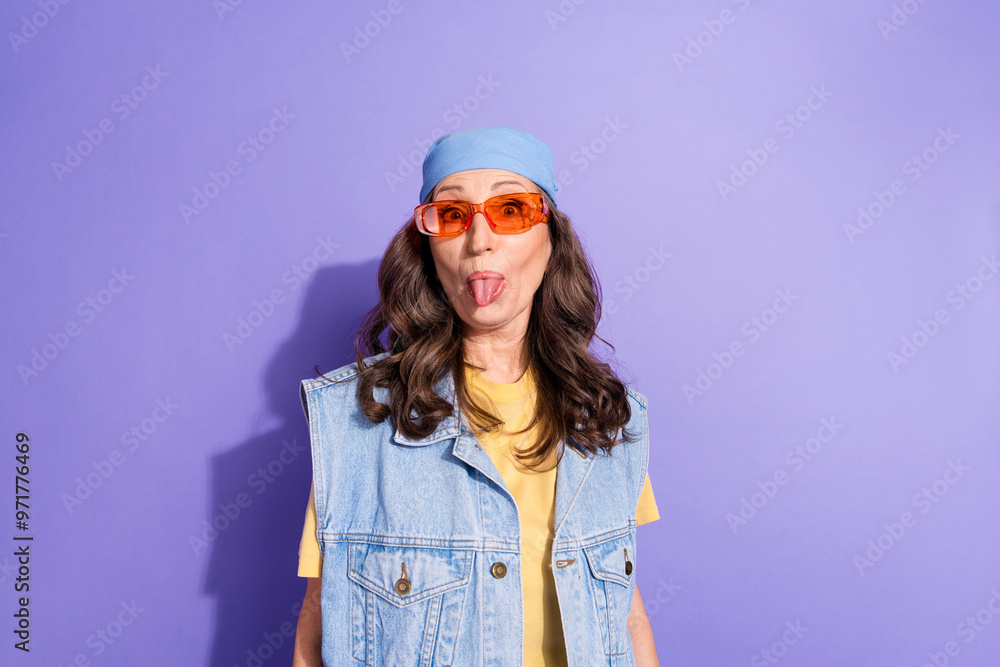 Photo portrait of pretty retired woman stick tongue out wear trendy denim hipster outfit isolated on violet color background Photo portrait of pretty retired woman stick tongue out wear trendy denim hipster outfit isolated on violet color background