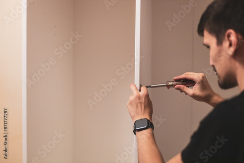 A young man is tightening the screws on the fittings inside the wardrobe.