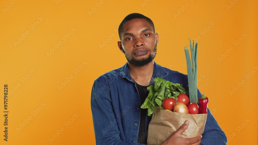 Portrait of african american guy holding a paper bag full of bio food, buying organic locally grown fruits and vegetables. Confident vegan person supporting healthy eating and zero waste. Camera A. Portrait of african american guy holding a paper bag full of bio food, buying organic locally grown fruits and vegetables. Confident vegan person supporting healthy eating and zero waste. Camera A.