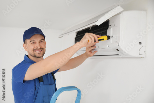 Male technician with screwdriver repairing air conditioner in room