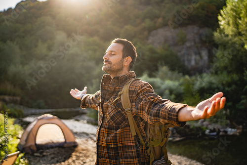 Adult man hiker with a backpack rise up his hands and enjoy the sun photo