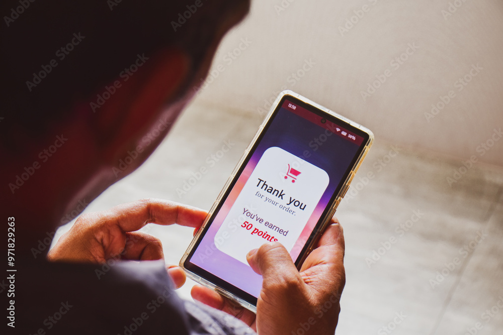 Fototapeta premium Smartphone screen showing a man earned 50 reward points by shopping online. E-commerce loyalty program concept, selective focus.