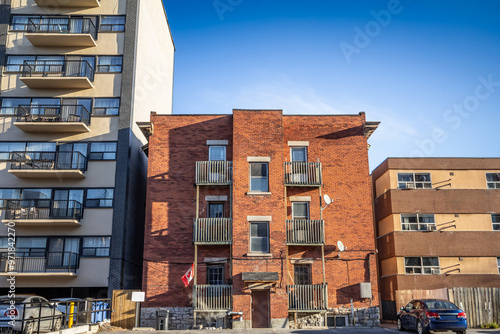 A neglected small apartment building on a residential street in Ottawa, Ontario, during an autumn afternoon. The building is surrounded by parked cars, showcasing an urban neighborhood in need of revi