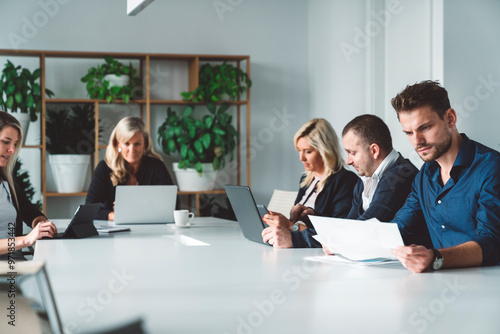 Group of colleagues working on laptops and digital tablets in conference room