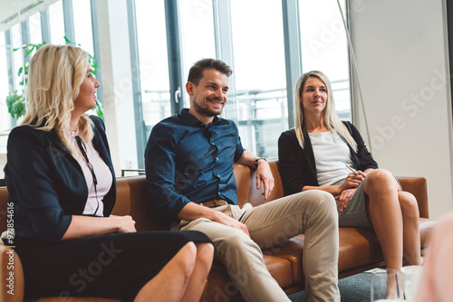 Group of three colleagues sitting on the sofa in office lounge having a discussion