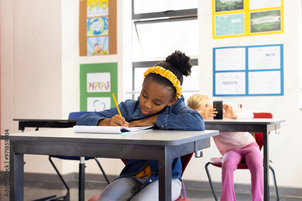 In school, african american girl writing in notebook at desk, focusing on her work In school, african american girl writing in notebook at desk, focusing on her work