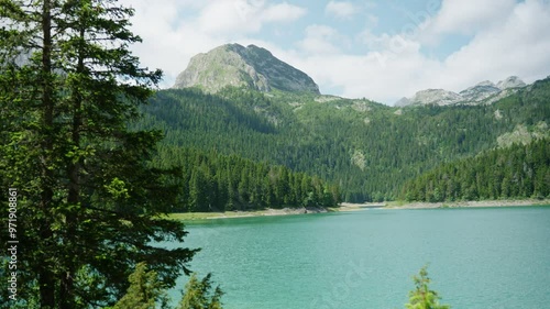 Wide shot of Black Lake Crno Jezero in Montenegro during summer or spring. Beautiful turquoise snow water alongside green lush vegetation and tall pine trees. Tourist attraction for hikers and bikers photo