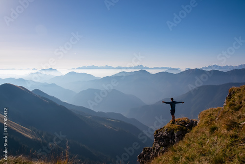 Silhouette of hiker man in alpine landscape of Gailtal Alps, Carinthia, Austria. Panoramic view of majestic hazy mountain ridges of Julian Alps, Karawanks, Carnic Alps. Peaceful tranquil atmosphere photo