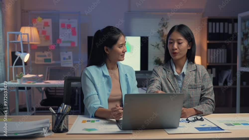 Two female managers work late in the office, collaborating over a laptop. Engaged in discussion, they analyze data and strategize for upcoming projects, showcasing teamwork and determination Two female managers work late in the office, collaborating over a laptop. Engaged in discussion, they analyze data and strategize for upcoming projects, showcasing teamwork and determination