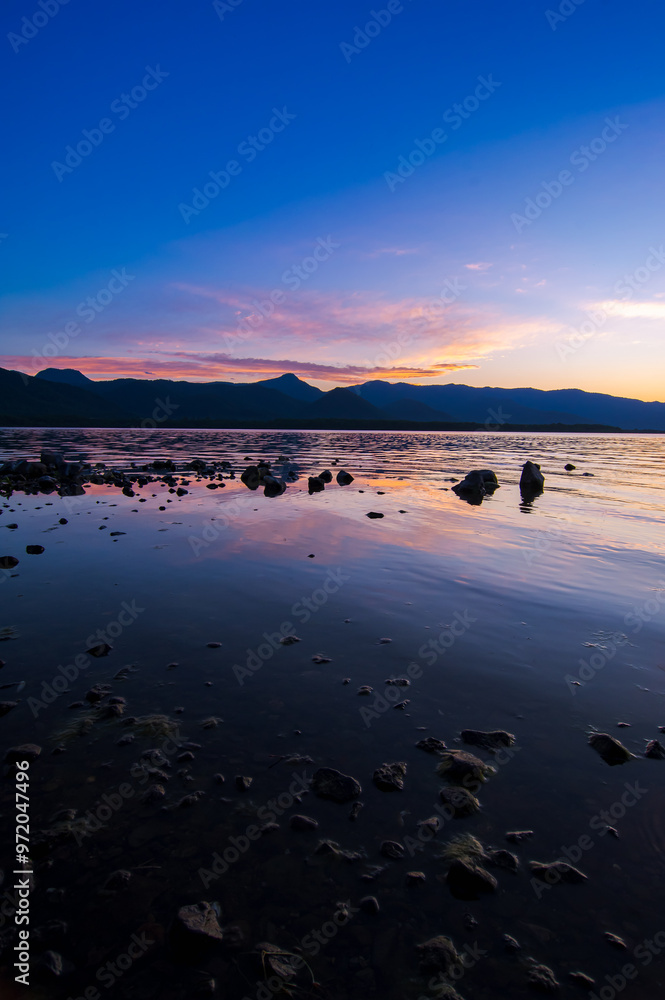 Fototapeta premium 鮮やかなグラデーションの空の色を湖面に反射する夕暮れの湖。岸辺からのローアングル。北海道の屈斜路湖。