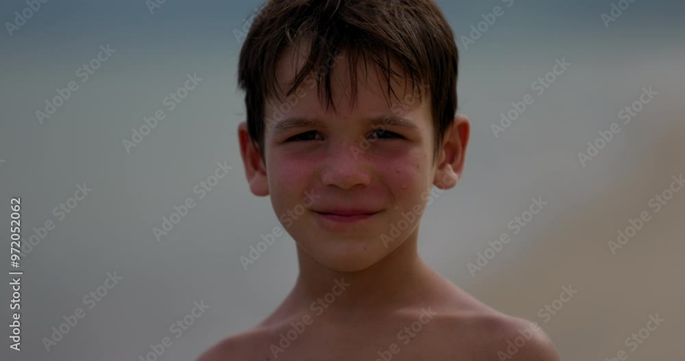 Young boy looks directly into camera with smirk on tropical beach - close up on face Young boy looks directly into camera with smirk on tropical beach - close up on face