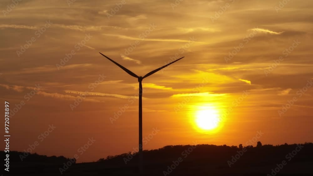Aerial view of wind turbine silhouetted against a golden sunset. The video captures the peaceful beauty of renewable energy in harmony with nature. (4K) Aerial view of wind turbine silhouetted against a golden sunset. The video captures the peaceful beauty of renewable energy in harmony with nature. (4K)