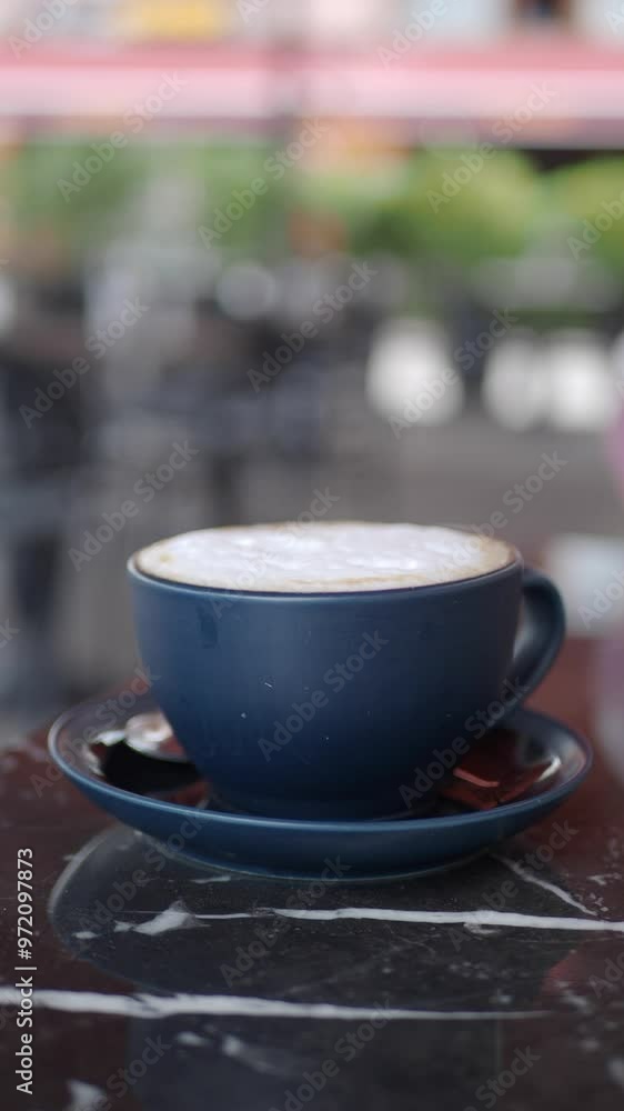 A delicious cappuccino presented beautifully in a blue cup placed on a stylish table A delicious cappuccino presented beautifully in a blue cup placed on a stylish table
