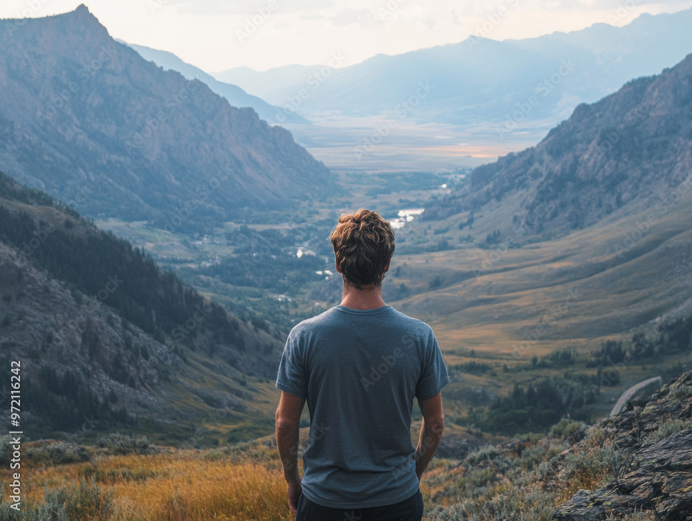 Fototapeta premium Man Contemplating Majestic Mountain View: A solitary figure stands on a mountaintop, gazing out at a breathtaking panorama of rolling hills and valleys. The image evokes a sense of awe, tranquility, a
