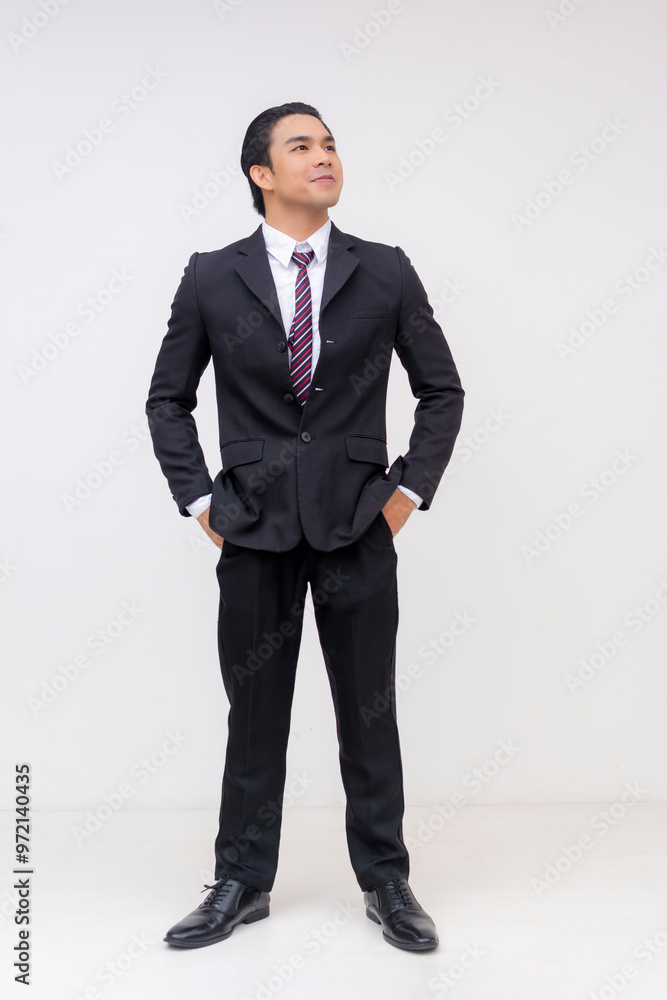Full-body Portrait of an ambitious young asian businessman in formal black suit and tie looking up with optimism, hands inside pockets. Isolated on a white background. Full-body Portrait of an ambitious young asian businessman in formal black suit and tie looking up with optimism, hands inside pockets. Isolated on a white background.