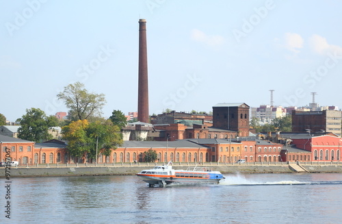 A tourist hydrofoil boat sails past the embankment with old brick industrial buildings, Oktyabrskaya Embankment of the Neva River, St. Petersburg, Russia, September 12, 2024 photo