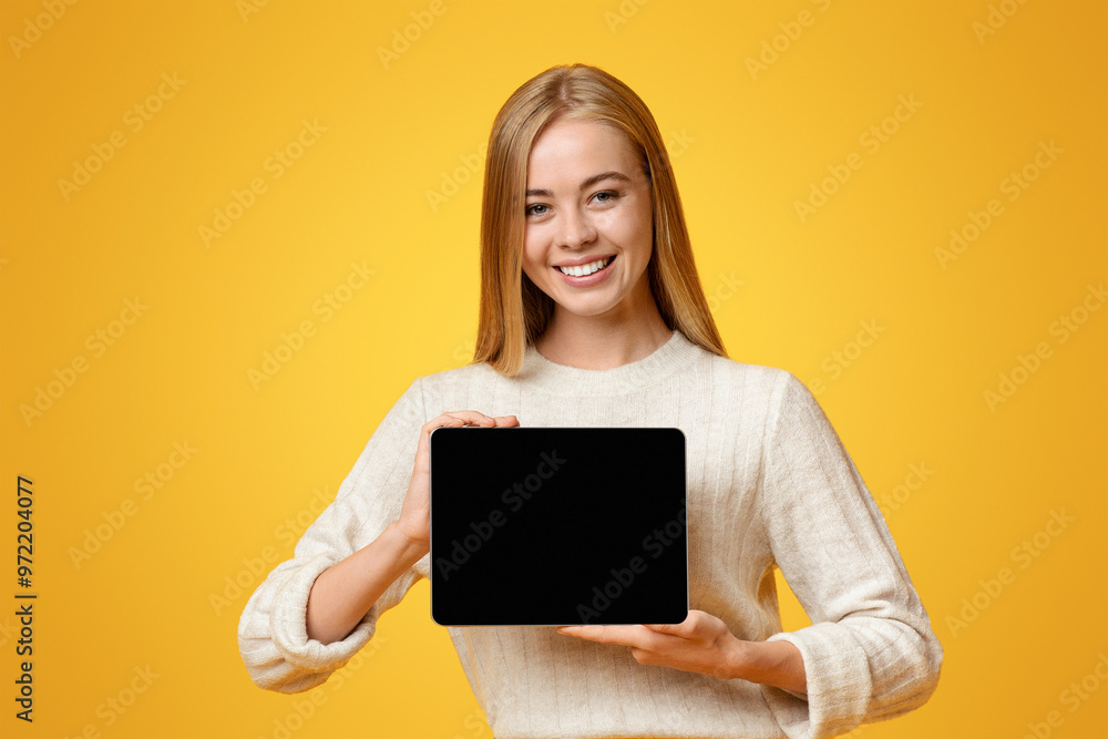 Naklejka premium Digital tablet with black blank screen in young girl's hands, orange backgroung with free space