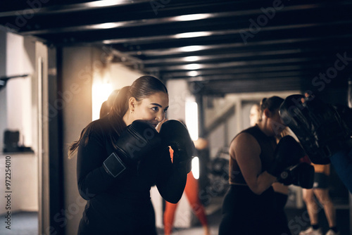 Fit young woman wearing sportswear and boxing gloves focused on a punching workout during a boxing class with others at the gym photo