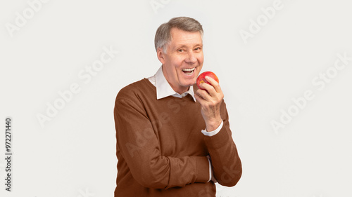 Smiling Senior Man Biting Apple Standing Over White Studio Background. Healthy Teeth In Old Age. Panorama, Free Space photo