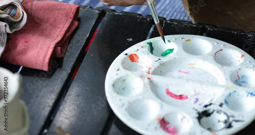 Hands of a Beautiful artist lady and artist painting together at a colorful table, surrounded by basket, brushes, acrylic colors tube and craft materials,Wicker handmade from krachut , Close up shot. photo