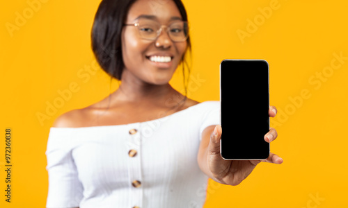 Black Girl Showing Phone Empty Screen Smiling At Camera Standing Over Orange Studio Background. Selective Focus, Mockup