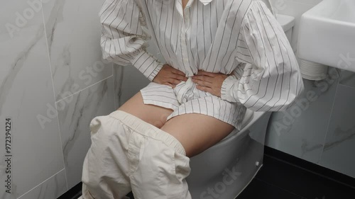 close up woman sitting on toilet bowl and holding her painful Stomach in the bathroom