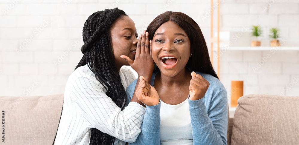 Fresh gossips. Young afro woman sharing secret with friend, whispering to her ear, sitting on sofa at home together. Fresh gossips. Young afro woman sharing secret with friend, whispering to her ear, sitting on sofa at home together.